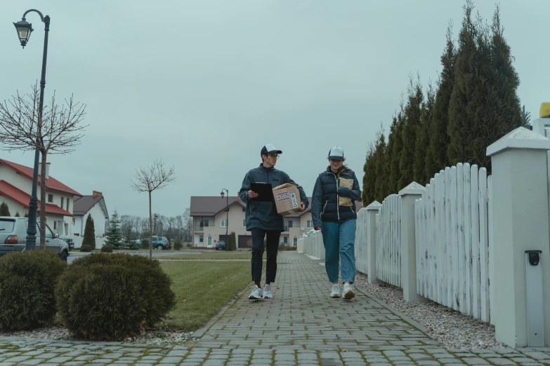 a couple of people walking down a sidewalk, by Emma Andijewska, pexels contest winner, realism, delivering mail, suburb, ready to eat, streetwear