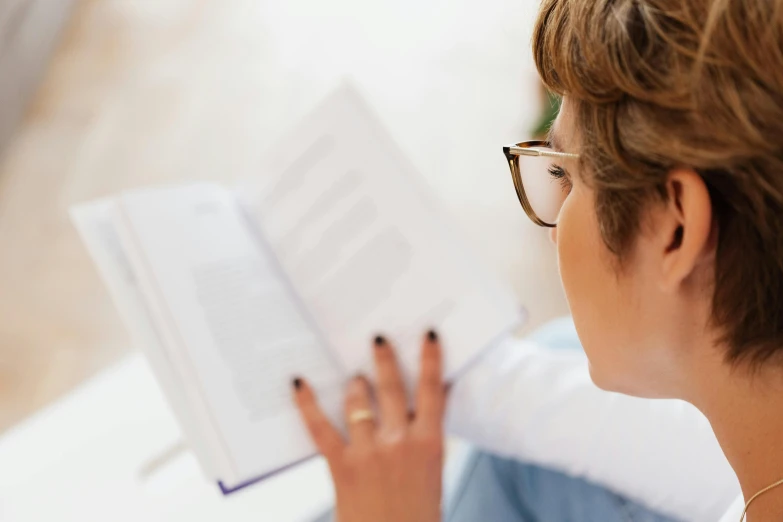 a woman sitting on a couch reading a book, by Nicolette Macnamara, pexels contest winner, white reading glasses, profile image, dynamic closeup, avatar image