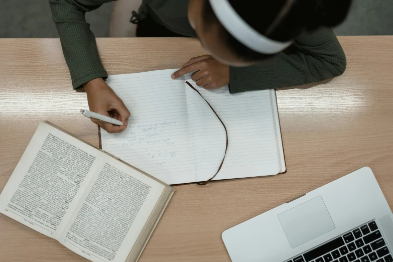 a woman sitting at a table with a book and a laptop, a drawing, pexels contest winner, lined paper, private school, riyahd cassiem, a high angle shot