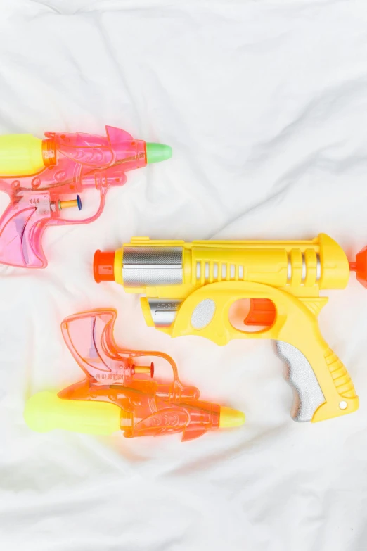 a couple of water guns laying on top of a bed, plastic toy, bullet tracers, high quality product image”, high angle shot