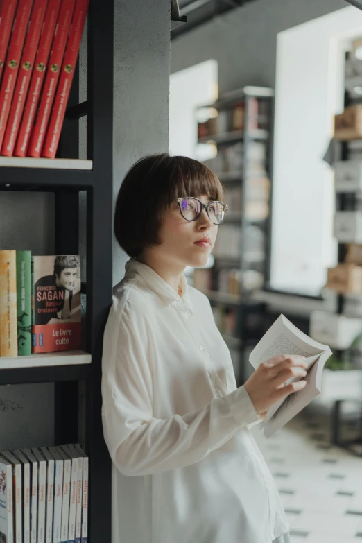 a woman standing in front of a book shelf holding a book, pexels contest winner, modernism, wearing white shirt, girl with glasses, pondering, gif