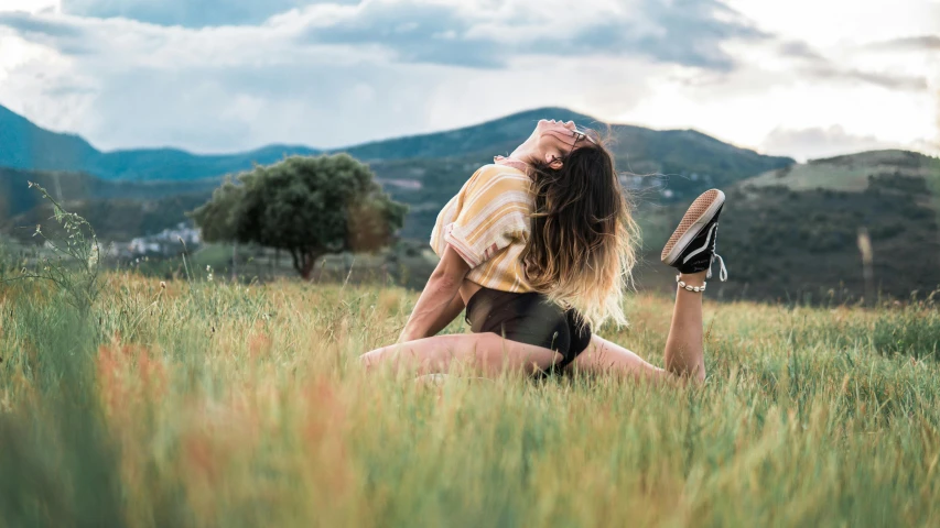 a woman sitting on top of a lush green field, pexels contest winner, figuration libre, doing splits and stretching, profile image, hills in the background, avatar image