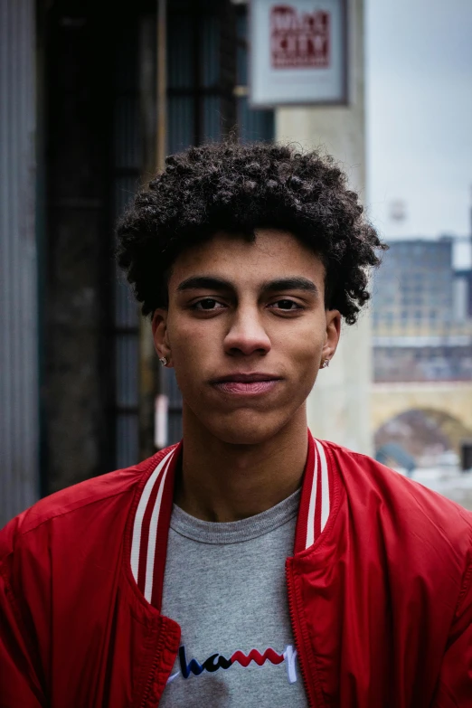 a man in a red jacket standing in front of a building, black teenage boy, curly and short top hair, portrait featured on unsplash, square masculine facial features