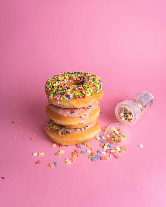 a pile of donuts with sprinkles on a pink background, by Cosmo Alexander, pexels, salt shaker, rainbow liquids, background image, 2 3 years old