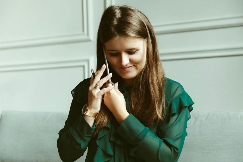 a woman sitting on a couch talking on a cell phone, by Emma Andijewska, pexels contest winner, copper and emerald jewelry, green tunic, smooth tiny details, young business woman