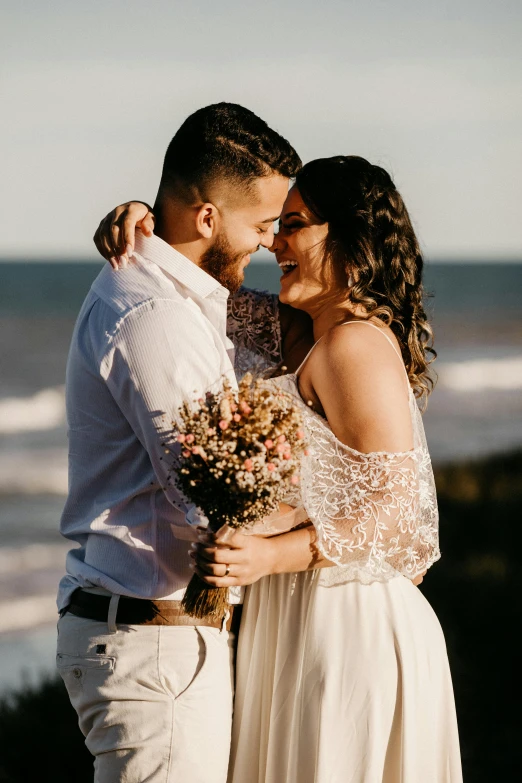 a man and woman standing next to each other on a beach, bouquets, with backdrop of natural light, hair, manly