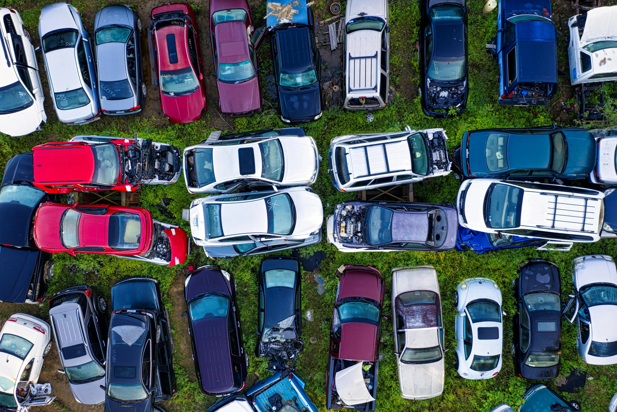 a group of cars sitting on top of a lush green field, trending on unsplash, auto-destructive art, crates and parts on the ground, drone photo, junk yard, brightly coloured