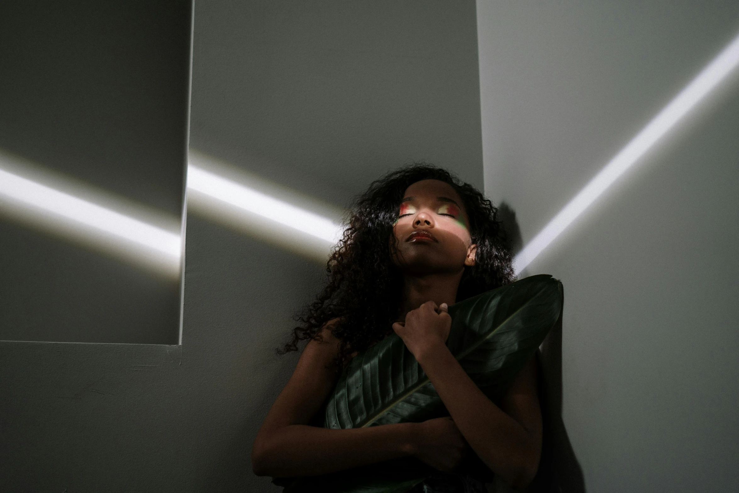 a woman in a green dress leaning against a wall, an album cover, pexels contest winner, light and space, dark-skinned, standing under a beam of light, soft light.4k, photograph of a techwear woman