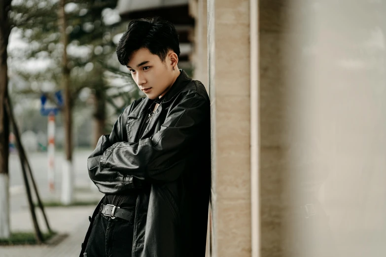 a man in a leather jacket leaning against a wall, trending on pexels, realism, young cute wan asian face, beautiful androgynous prince, background image, wearing dark robe