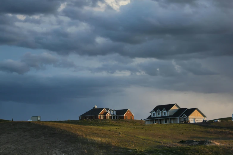 a couple of houses sitting on top of a hill, by Jessie Algie, unsplash contest winner, storm clouds in the distance, prairie, several cottages, evening lighting