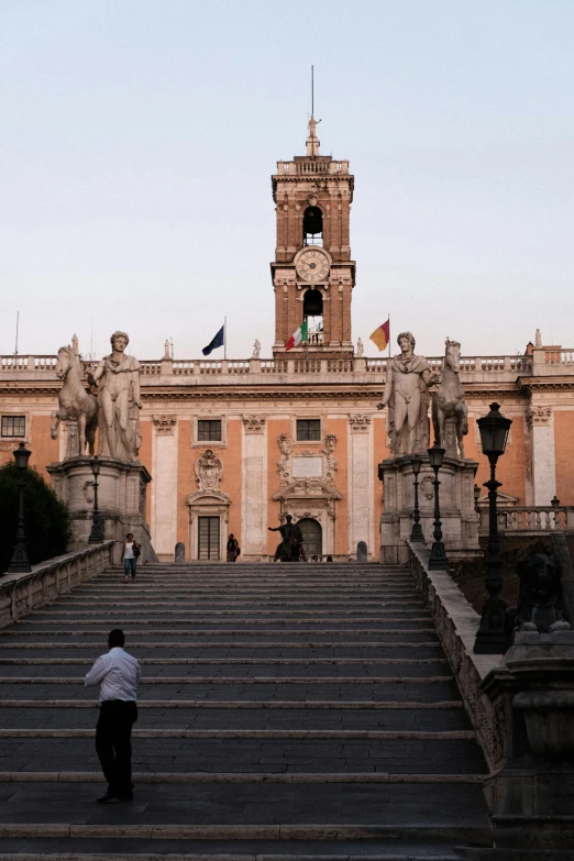 a man walking up a flight of stairs in front of a building, inspired by Vincenzo Cabianca, neoclassicism, at dusk, holy cross, staggered terraces, wide grand staircase