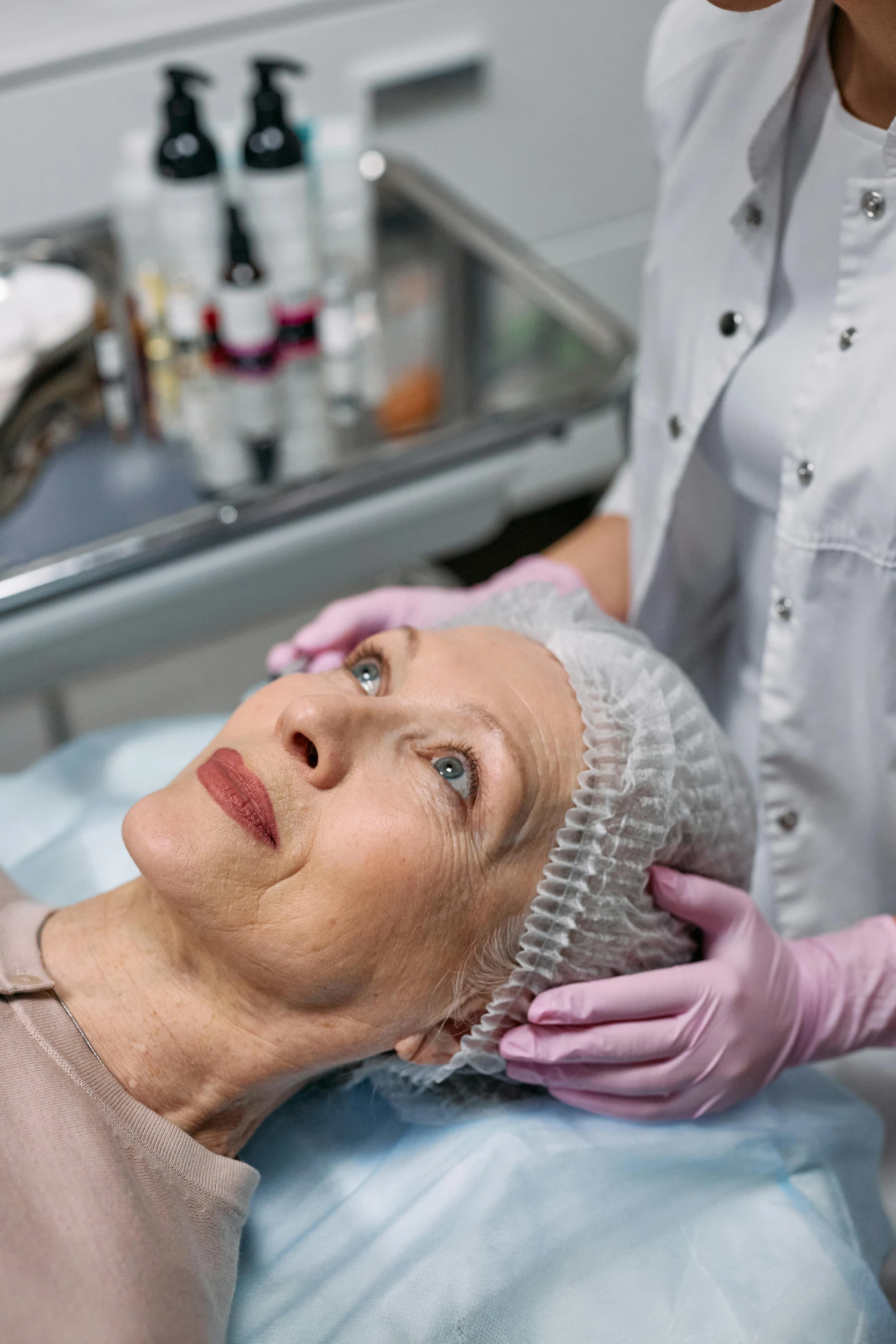 a woman getting her hair done by a hair stylist, a photo, by Julian Allen, renaissance, surgery theatre, wrinkly forehead, silicone skin, in hospital bed
