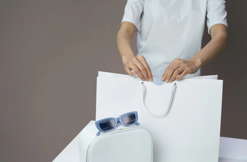 a woman holding a white bag and a pair of sunglasses, inspired by Gao Cen, minimalism, sleek oled blue visor for eyes, product view, excitement, white finish