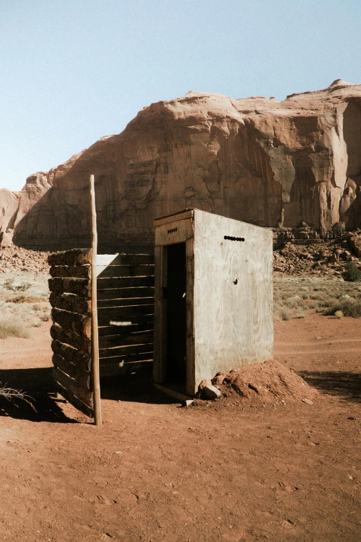 an outhouse in the desert with mountains in the background, by Jessie Algie, unsplash contest winner, land art, style of monument valley, crates and parts on the ground, empty bathhouse hidden in a cave, polaroid photo of trailerpark