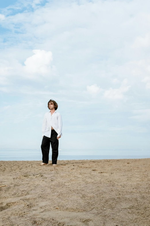 a man standing on top of a sandy beach, an album cover, by Nina Hamnett, happening, wearing a white shirt, looking off to the side, high resolution image, frank dillane