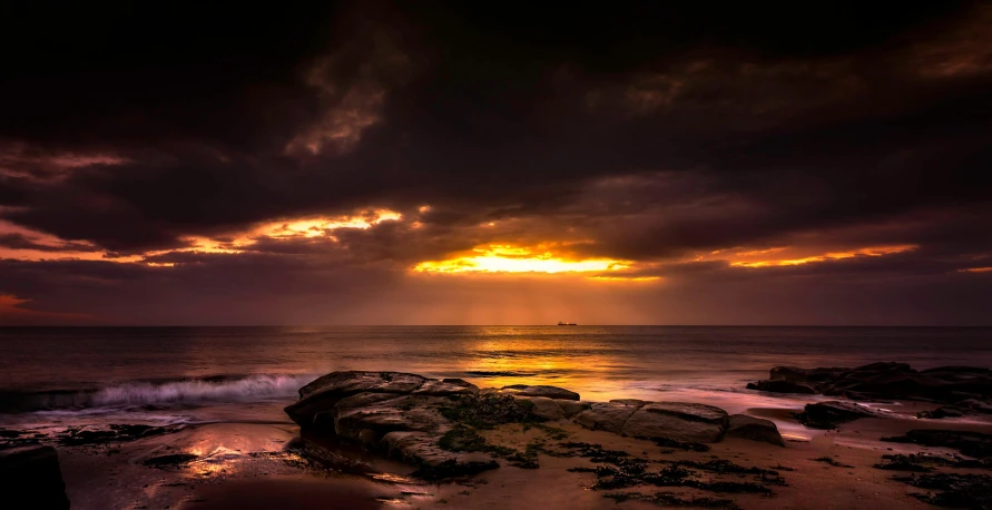 a large rock sitting on top of a sandy beach, by Peter Churcher, pexels contest winner, australian tonalism, crepuscular rays, golden clouds, manly, storm on horizon