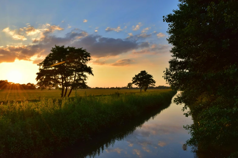 a river running through a lush green field, a picture, by Jan Tengnagel, pexels contest winner, renaissance, tree-lined path at sunset, canal, thumbnail, summer sky