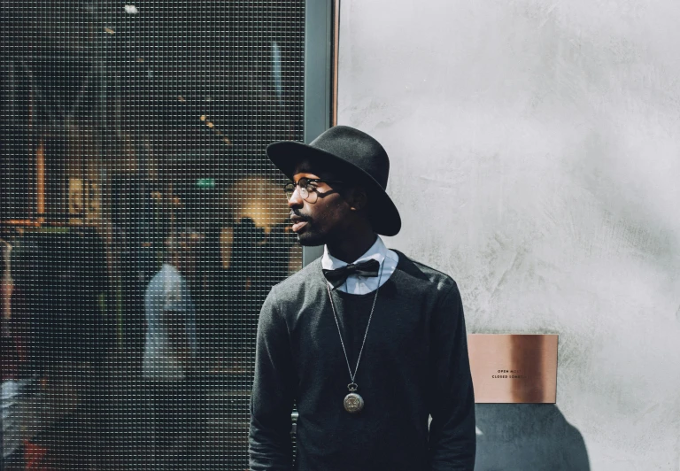 a man standing in front of a window wearing a hat, inspired by Theo Constanté, pexels contest winner, black jewelry, lil uzi vert, wearing a suit and glasses, helsinki