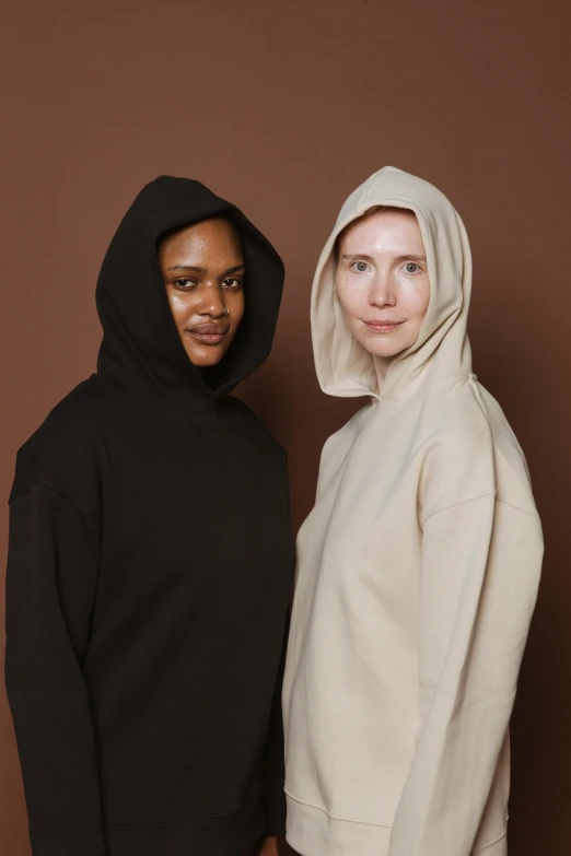 a couple of women standing next to each other, by Matija Jama, beige hoodie, in a black hoodie, varying ethnicities, skincare