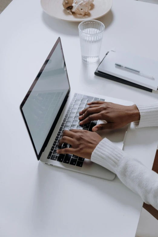 a woman sitting at a table using a laptop computer, a computer rendering, by Carey Morris, trending on unsplash, wearing a white sweater, on grey background, sleek hands, afro tech