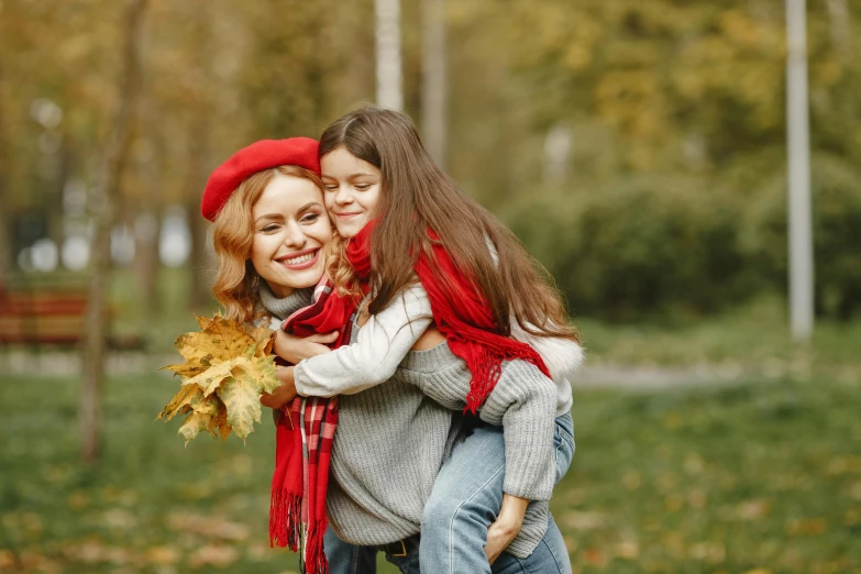 a woman carrying a little girl in her arms, a picture, shutterstock, grassy autumn park outdoor, red cap, square, avatar image