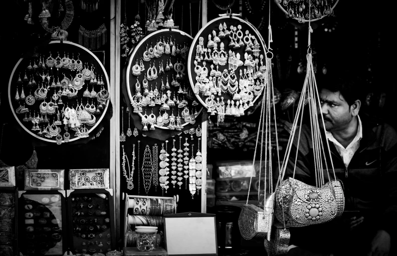 a black and white photo of a man sitting in front of a store, maximalism, dreamcatchers, intricate jewellery, lacquerware, bw photo