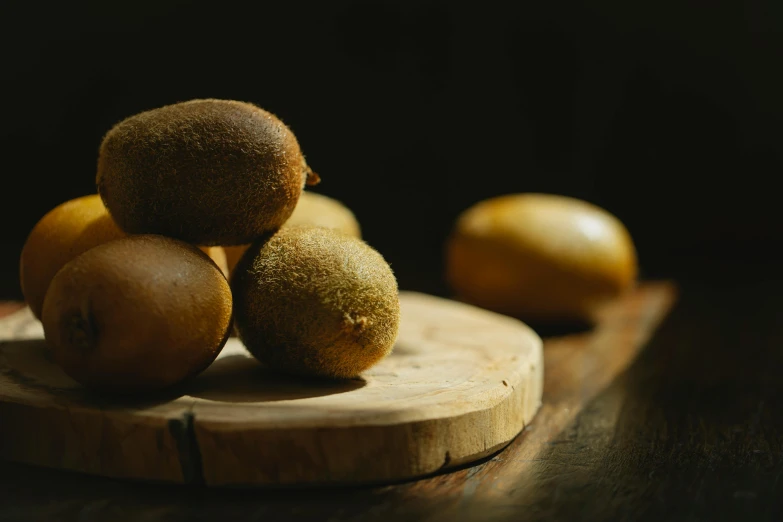 a pile of kiwis sitting on top of a wooden cutting board, a still life, inspired by Kanō Naizen, unsplash, muted brown yellow and blacks, smooth oval head, thumbnail, award winning dark