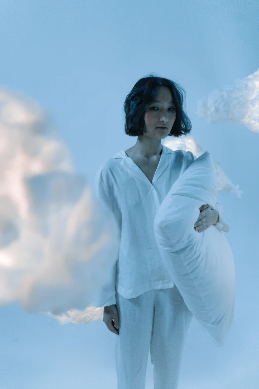 a woman holding a pillow in front of a cloud, inspired by Anna Füssli, conceptual art, wearing white pajamas, zoe kravitz as an astronaut, cryogenic pods, soft blue light