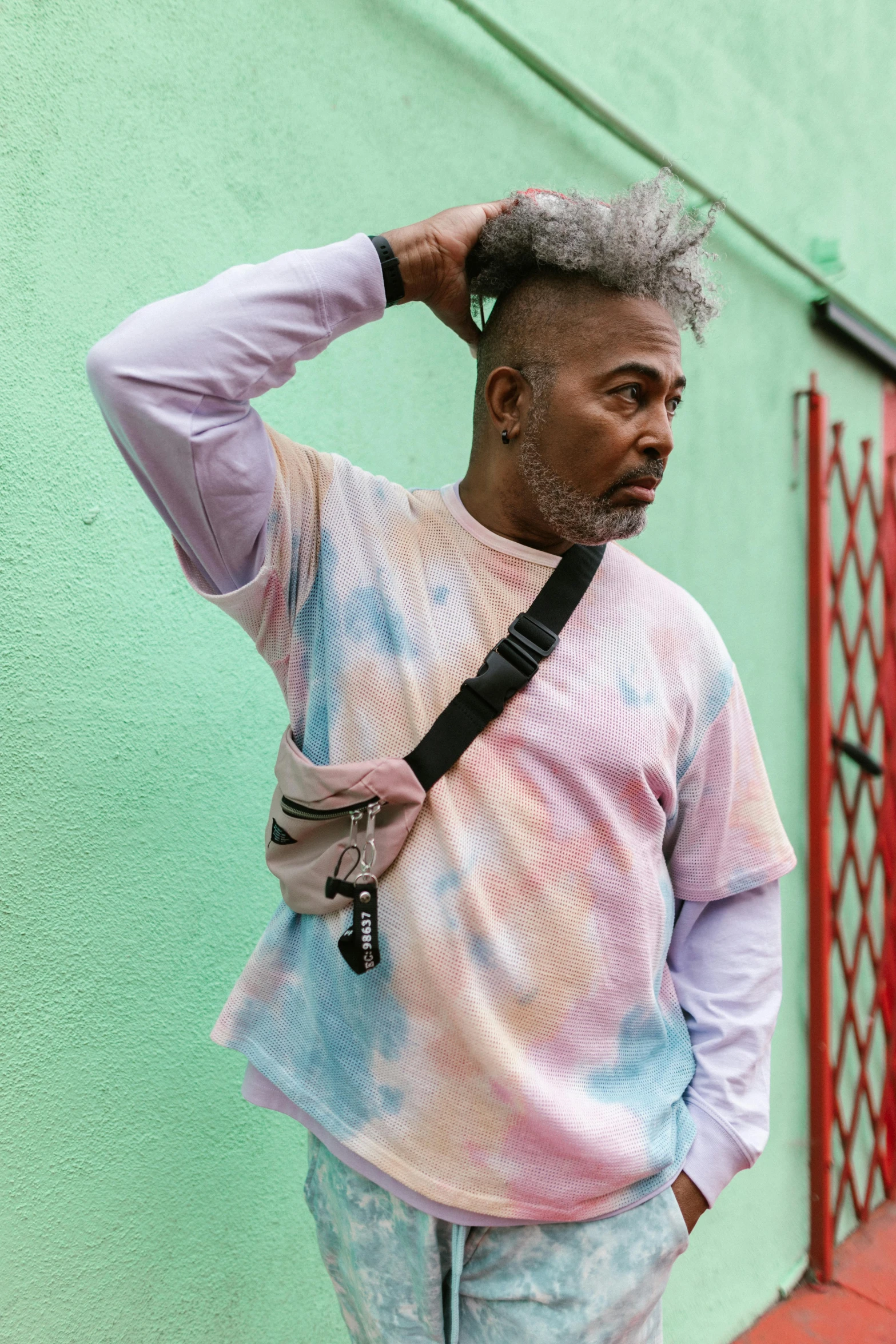 a man standing in front of a green wall, a photo, inspired by Frank Mason, trending on pexels, tie die shirt, cloudy grey hair, afropunk, pastel faded grey rainbow