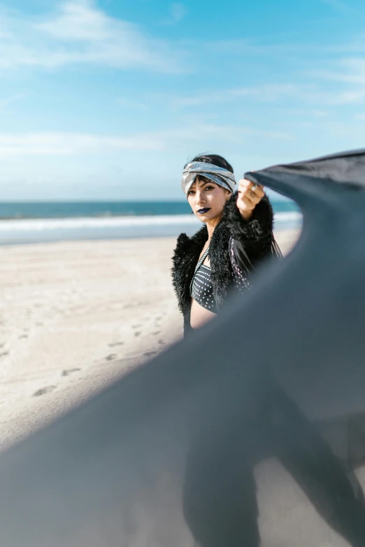 a woman standing on a beach holding a surfboard, an album cover, unsplash, wrapped in a black scarf, turban, fashion shoot 8k, road trip