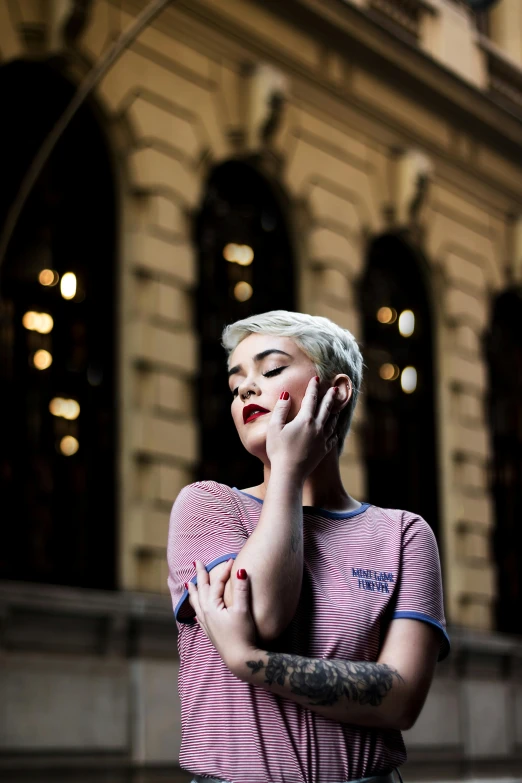 a woman talking on a cell phone in front of a building, an album cover, inspired by Elsa Bleda, pexels contest winner, happening, short white hair shaved sides, bisexual lighting, sydney hanson, hand on cheek