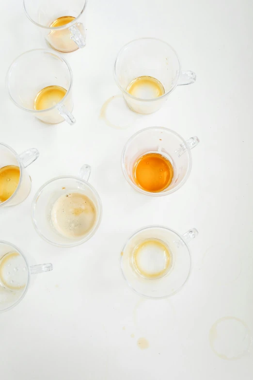 a bunch of cups sitting on top of a table, by Jessie Algie, trending on unsplash, process art, liquid translucent amber, on white, soup, high angle close up shot