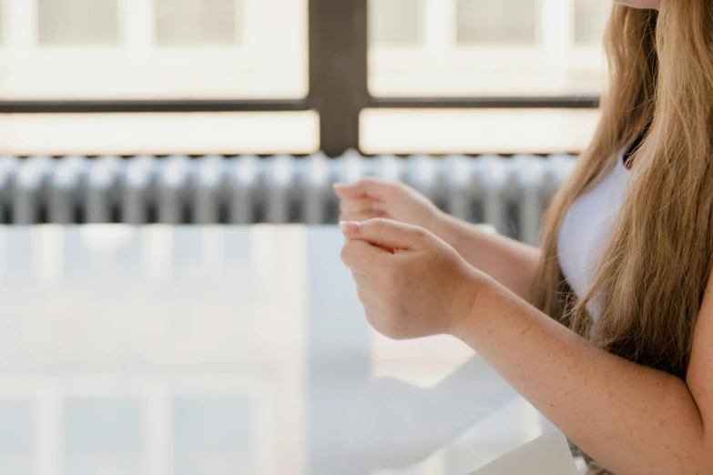 a close up of a person using a cell phone, sitting on a table, a girl with blonde hair, wearing a white button up shirt, unclipped fingernails