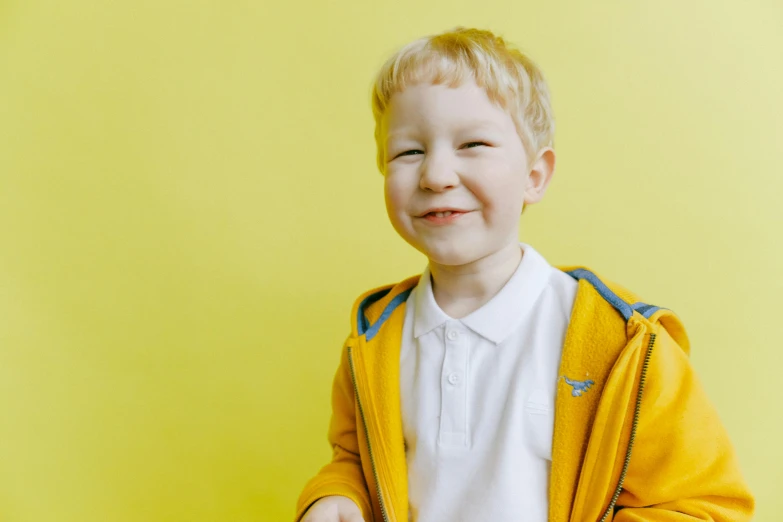 a young boy standing in front of a yellow wall, pexels, wearing a school uniform, a blond, he is smiling, bright: