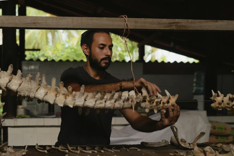 a man standing in front of a rack of bones, process art, sri lanka, using leather armour with bones, profile image, in a workshop