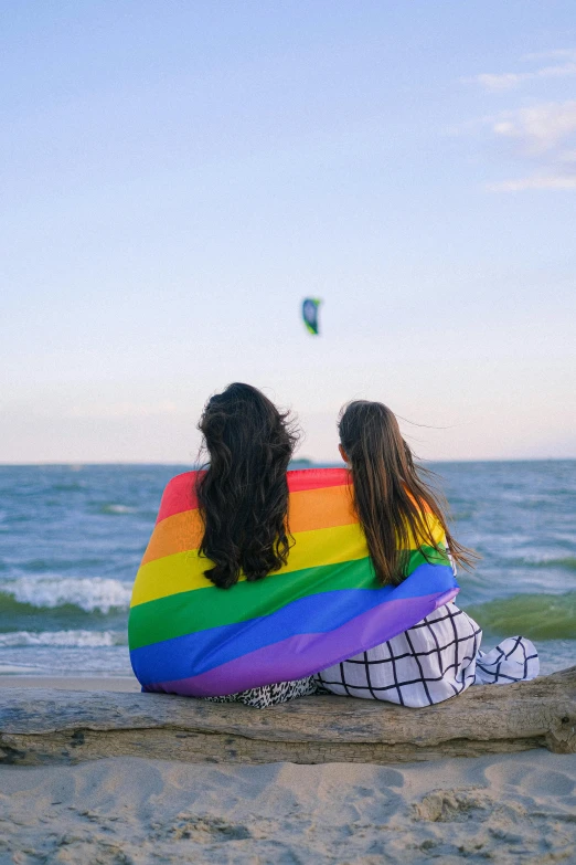 a couple of women sitting on top of a sandy beach, lgbt flag, trending on gc society, kites, profile image