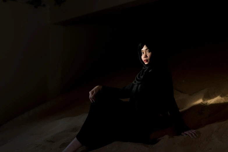 a woman sitting in the sand in a dark room, by Maryam Hashemi, wearing black clothes, ameera al taweel, miyamoto abduzeedo, promo image