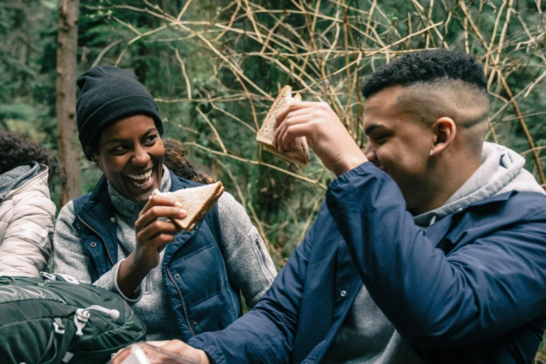 a group of people sitting next to each other eating food, by Joe Bowler, pexels contest winner, forest picnic, holding toasted brioche bun, avatar image, laughing menacingly