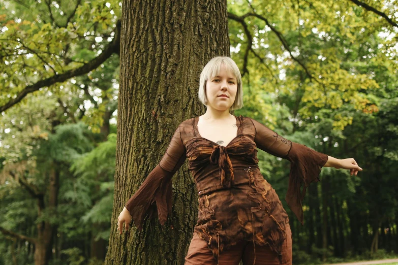 a woman standing next to a tree in a park, an album cover, inspired by Jane Nasmyth, renaissance, wooden bark armor, wearing atompunk jumpsuit, in lace brown dress, nina tryggvadottir