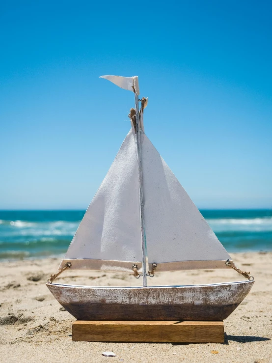 a small sailboat sitting on top of a sandy beach, inspired by Willem van de Velde the Elder, unsplash, new sculpture, white beard, wooden bowl, family friendly, medium wide front shot