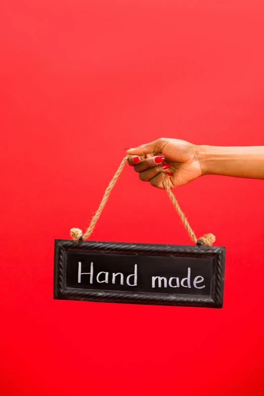 a hand holding a sign that says hand made, by Alice Mason, trending on pexels, made of smooth black goo, two hang, thumbnail, small manufacture