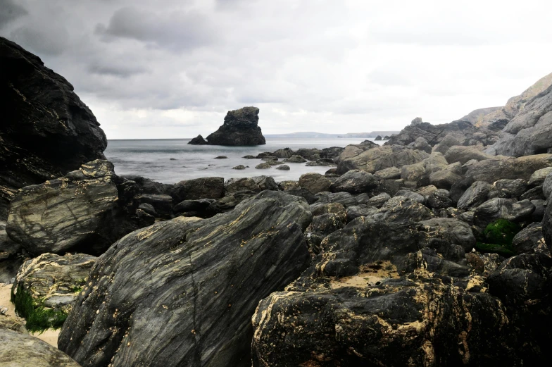 a group of rocks sitting on top of a rocky beach, an album cover, inspired by Thomas Struth, unsplash, romanticism, grey sky, pembrokeshire, geological strata, quixel megascans