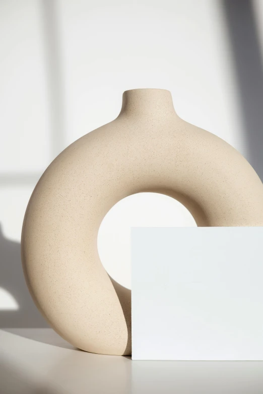 a vase sitting on top of a table next to a white card, inspired by Isamu Noguchi, trending on unsplash, new sculpture, beige cream natural muted tones, enso, side view intricate details, arched back