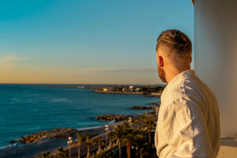 a man standing on a balcony looking out at the ocean, by Julia Pishtar, pexels contest winner, warm glow, cannes, widescreen, fan favorite
