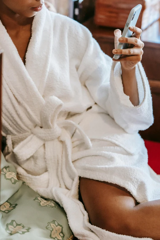 a woman sitting on a bed holding a cell phone, dirty linen robes, with a drink, wearing a wet white short dress, zoomed in shots