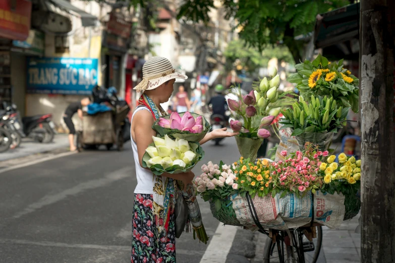 a woman selling flowers on the side of the road, a photo, riding a motorbike down a street, square, profile image, conde nast traveler photo