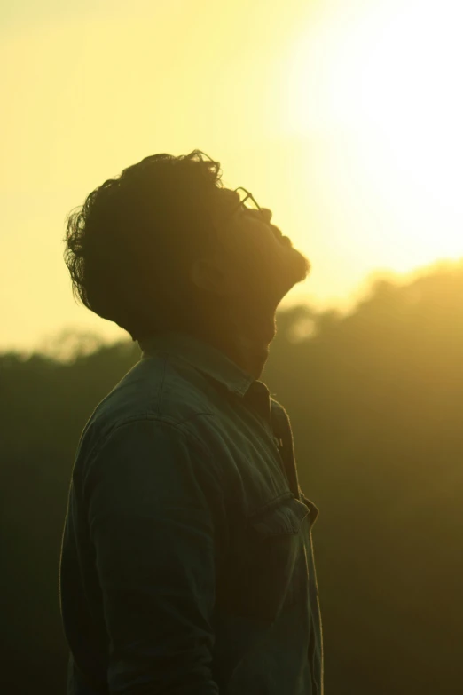 a man standing in front of a sunset, movie still of a tired, jayison devadas, backlit golden hour, head bowed slightly