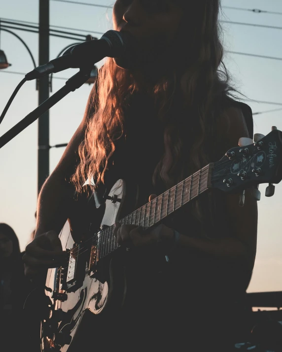 a woman playing a guitar in front of a microphone, pexels contest winner, antipodeans, at twilight, zoomed out, sydney hanson, kailee mandel