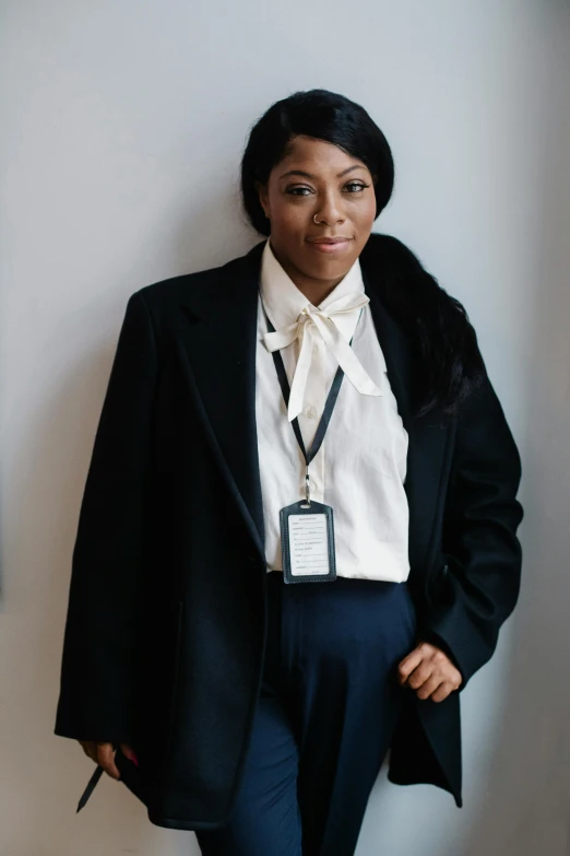 a woman standing in front of a white wall, an album cover, inspired by August Sander, unsplash, wearing robes and neckties, naomi campbell, wearing headmistress uniform, detective coat