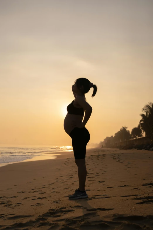 a pregnant woman standing on a beach at sunset, happening, with a sleek spoiler, malaysian, fitness, beaches